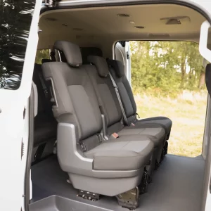 Erste Sitzreihe eines VW 9-Sitzers mit drei grauen Einzelsitzen und geöffnetem Schiebetürrahmen vor einer grünen Außenkulisse
