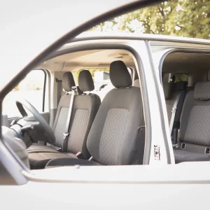 Innenansicht eines VW 9-Sitzers von der Seite mit geöffneten Türen und sichtbaren Sitzreihen mit grauen Polstersitzen